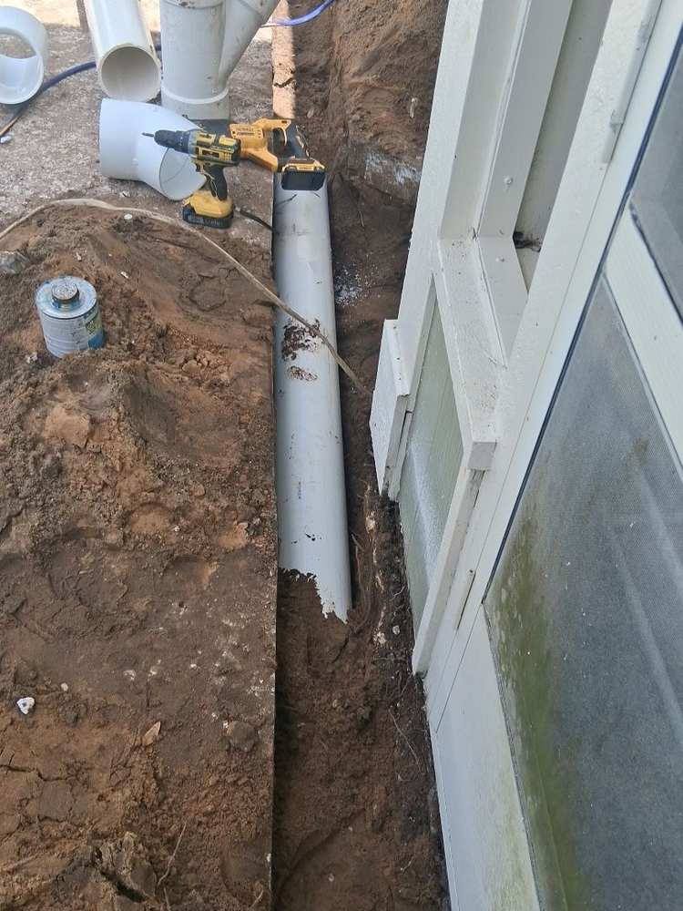 White rock filling a fabric-lined French drain trench along a wooden fence under palms