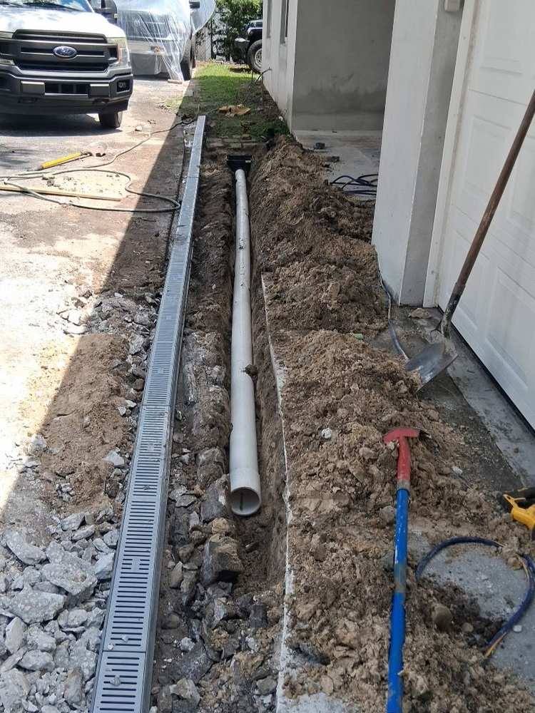 Drain pipe routed in a narrow trench past a blooming rose bed