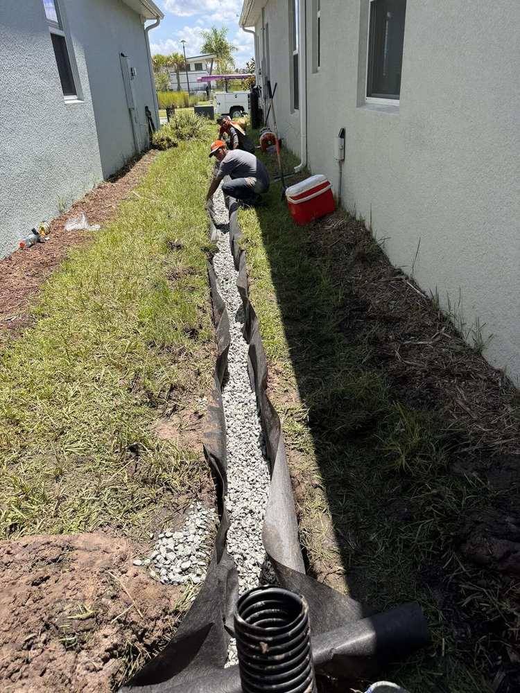 Crew placing washed rock into a fabric-lined French drain trench between two homes