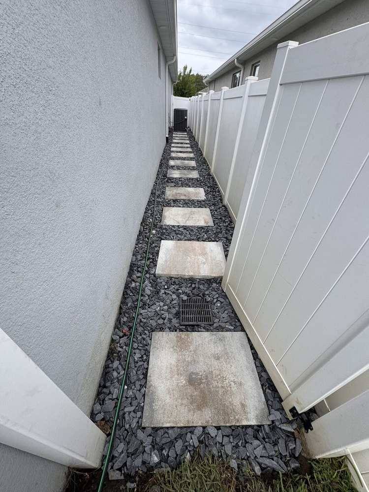 Stepping-stone path over drainage rock with an inline drain grate between house and fence