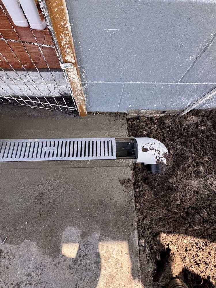 White PVC discharge elbow connected to a channel drain before backfill