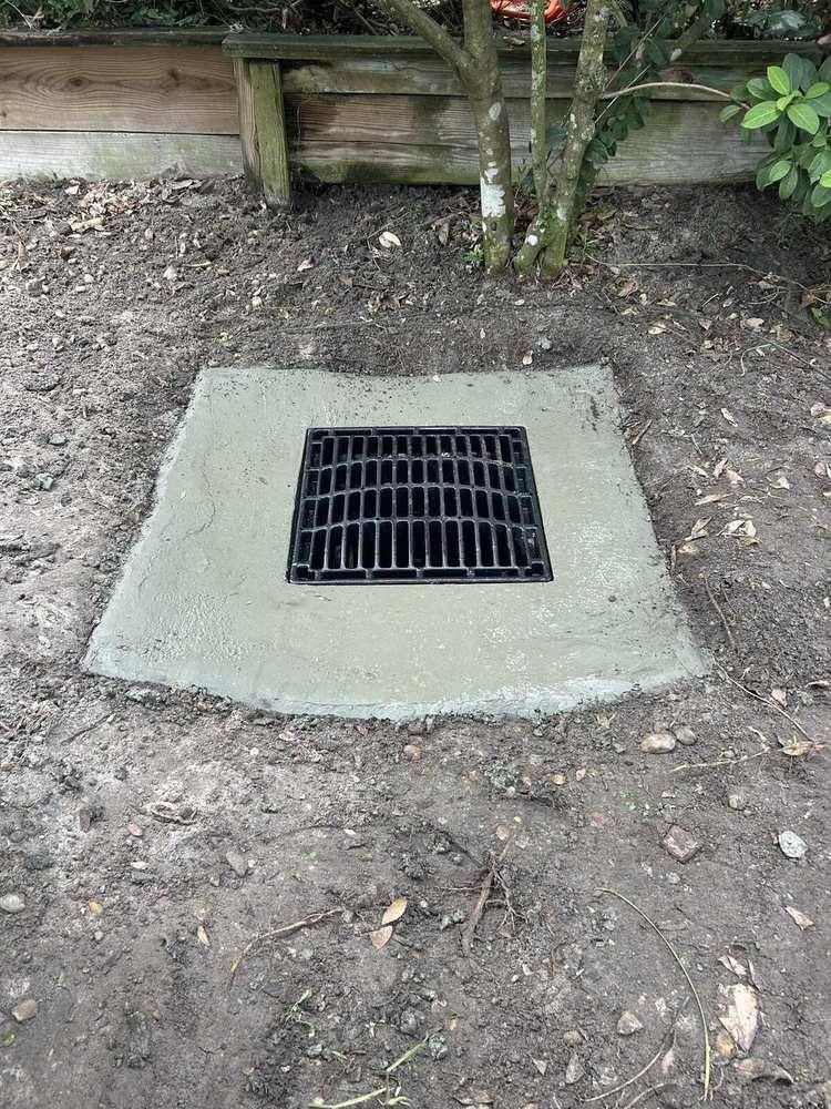 Square catch basin grate set in a concrete pad in a yard