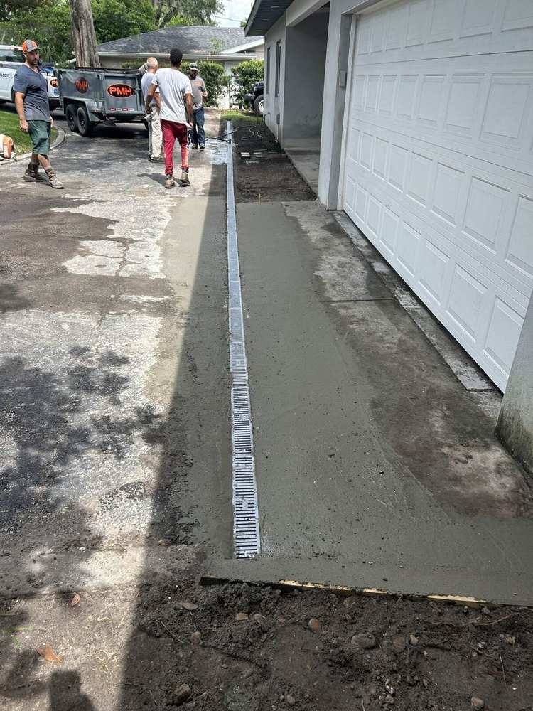 Channel drain run in fresh concrete along a full driveway, PMH trailer behind